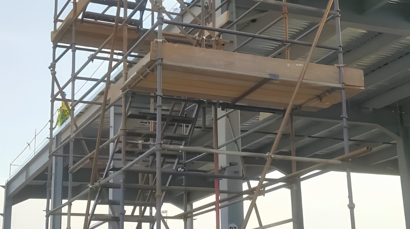 Tube-and-fitting scaffold with timber platform boards erected around a steel structure.